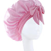 Pink silky satin sleep bonnet tied with a bow displayed on a white mannequin head.