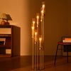 Centro de mesa alto y esbelto de candelero dorado con siete brazos verticales que sostienen velas encendidas.