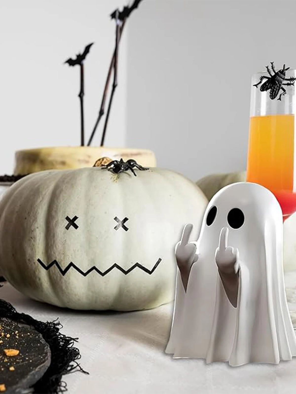 A white pumpkin decoration is shown next to a white ghost statue and a black spider.