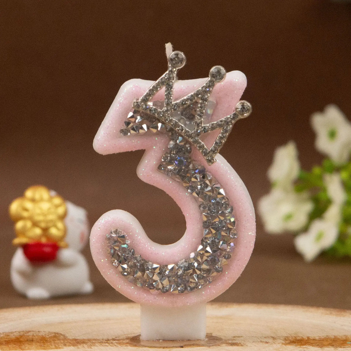 Pinke Dekoration, Kerze in Form der Ziffer 3 mit Diamantkrone auf Holzoberfläche.