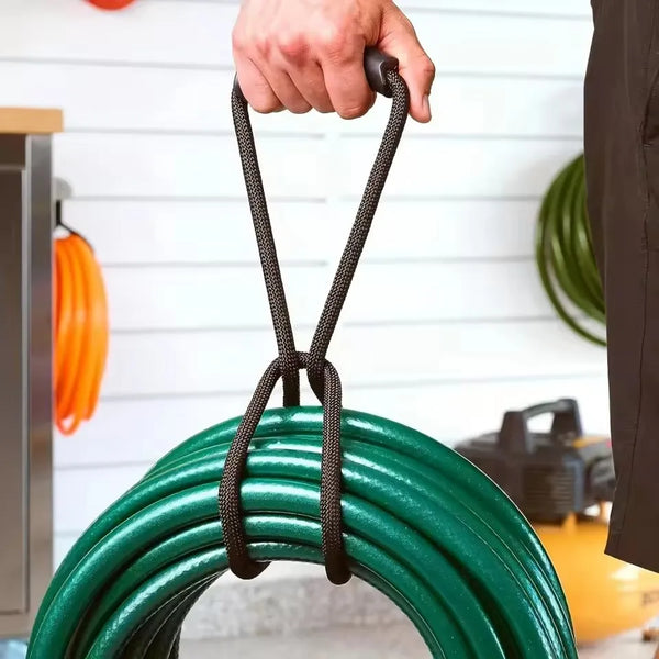A hand is holding a black hook and loop cord strap, which is used to organize a green hose or cord.