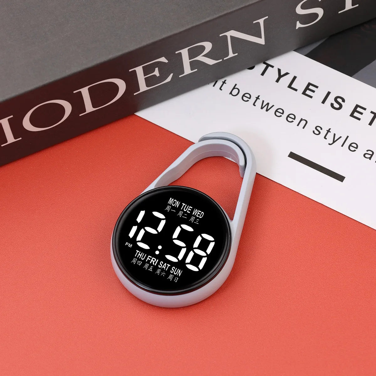 A white digital LED hanging pocket watch displaying 12:58 on a red surface.