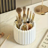 A white cylindrical organizer holds various makeup brushes and applicators on a marble surface.