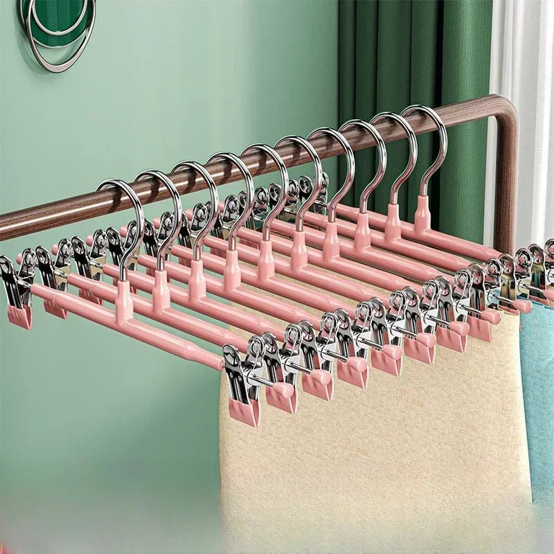 A rack of pink stainless steel adjustable clothing hangers displayed against a light green wall.