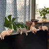 A set of three small, realistic cat figurines in various shades of beige and gray are displayed on a dark surface.