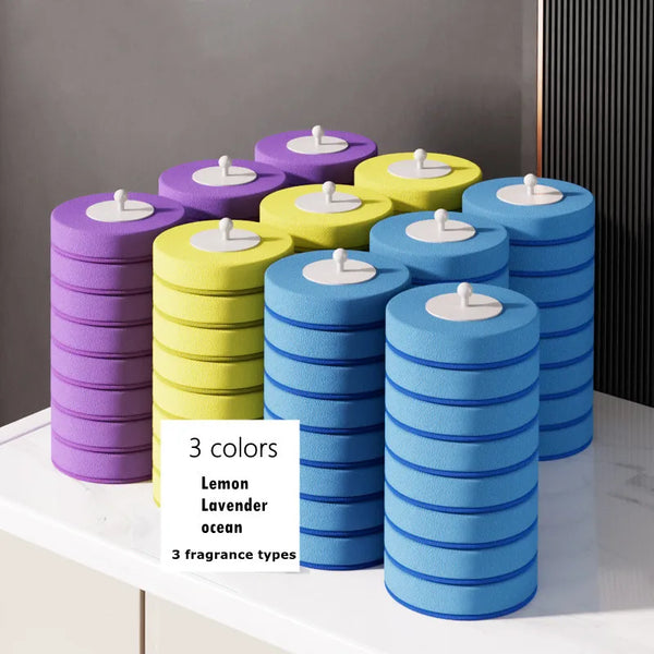 Three cylindrical purple, yellow, and blue disposable toilet brush heads displayed on a white surface.