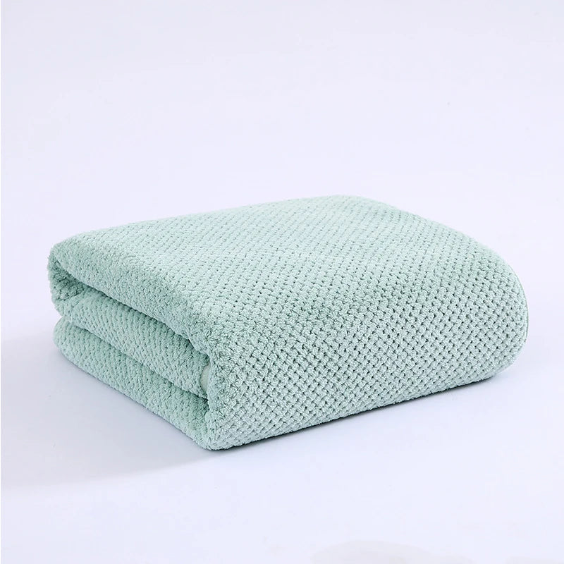A light mint green thickened microfiber bath towel folded neatly on a white surface.