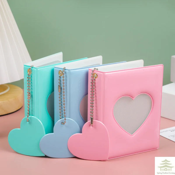 A set of three heart-shaped mini photo albums in teal, blue, and pink with gold chain closures.