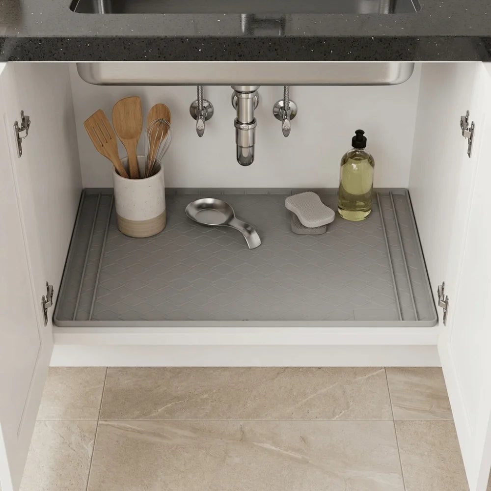 A silicone under sink waterproof mat is placed on a kitchen sink, with various utensils and a bottle visible.
