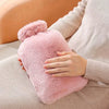 A hand warmer with a fluffy pink cloth cover is being held by a person wearing a beige sweater.