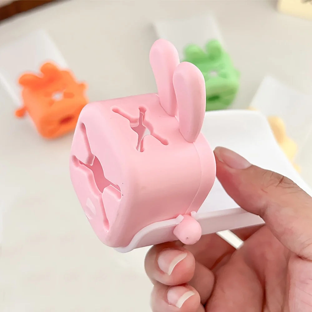 A hand holds a pink anti-splash faucet extender shaped like a cute rabbit against a white background.
