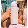 A person holds a pink Owala insulated water bottle with a straw against a light background.