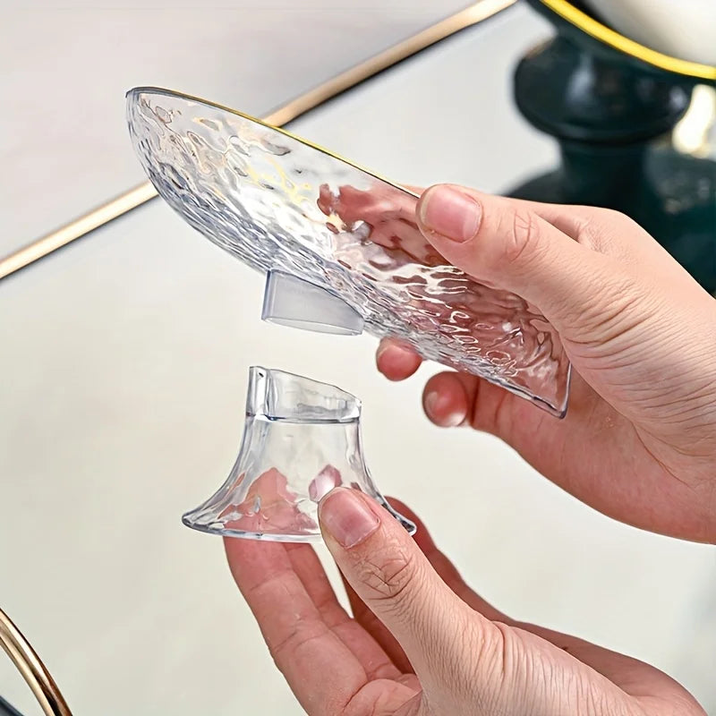 A hand is holding an oval clear plastic soap dish with drainage holes against a reflective surface.