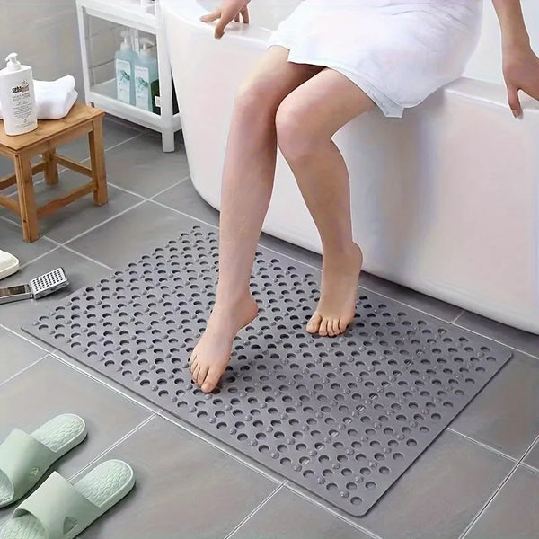 A gray anti-slip PVC shower mat with drainage holes placed on a tiled floor.