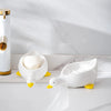 A white duck-shaped soap dish sits on a marble surface next to a gold dispenser.