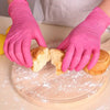 Hands wearing pink disposable nitrile gloves are slicing bread on a wooden cutting board.