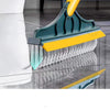 A close-up view of a teal and yellow 2-in-1 floor scrub brush being used to clean a reflective floor surface.