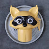 A yellow decorative toilet paper holder shaped like a fox head with black markings, sitting on a silver tray.