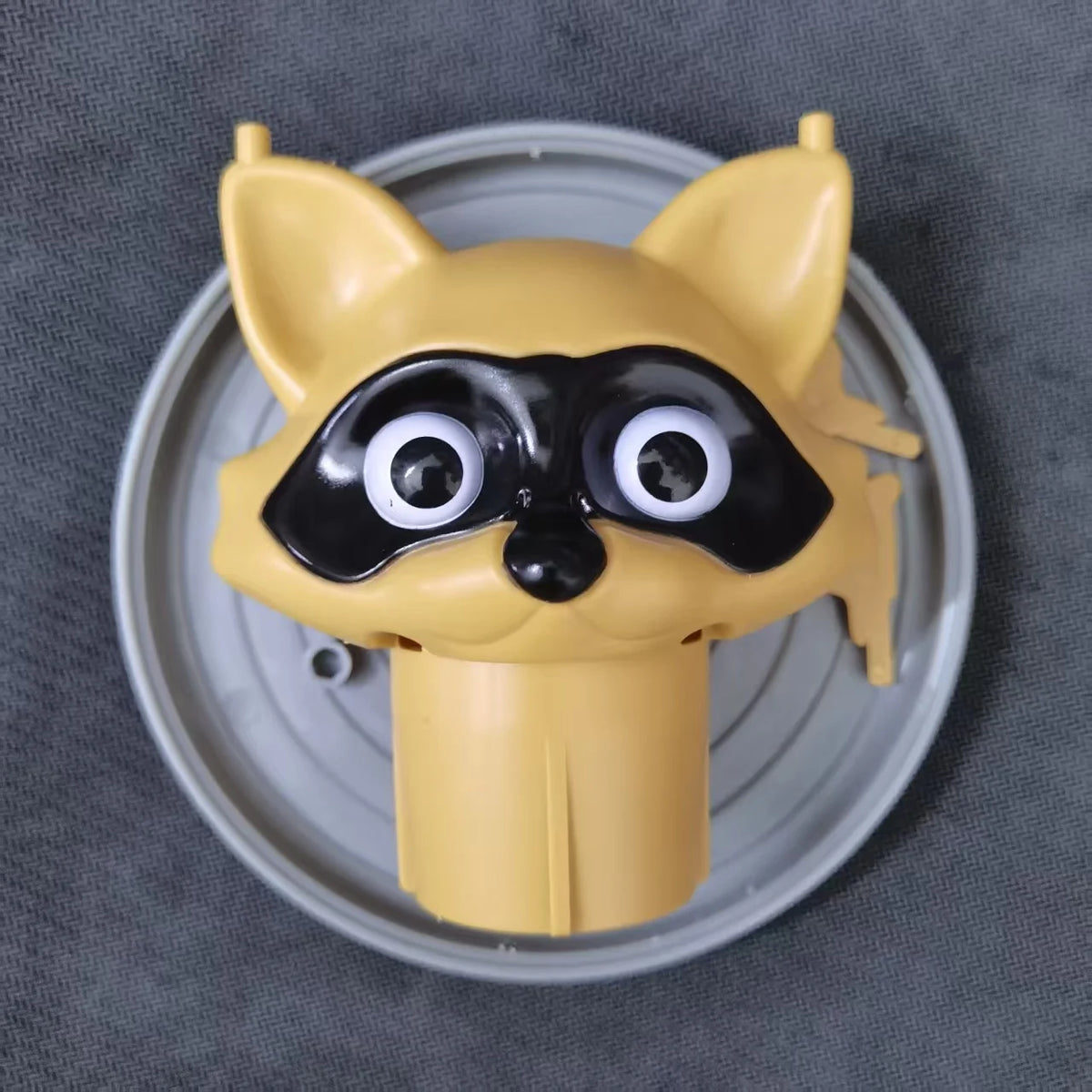 A yellow decorative toilet paper holder shaped like a fox head with black markings, sitting on a silver tray.