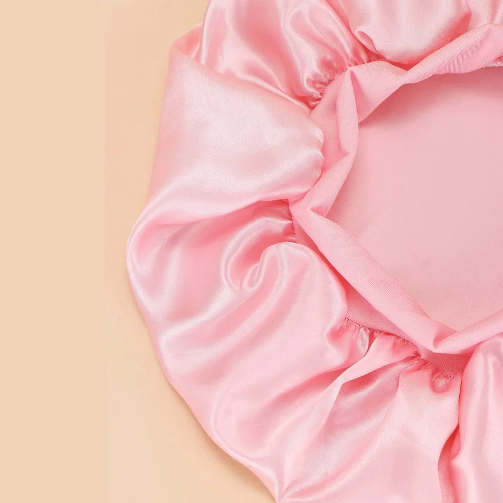 A pink satin wide brim shower cap is shown folded on a light beige background.