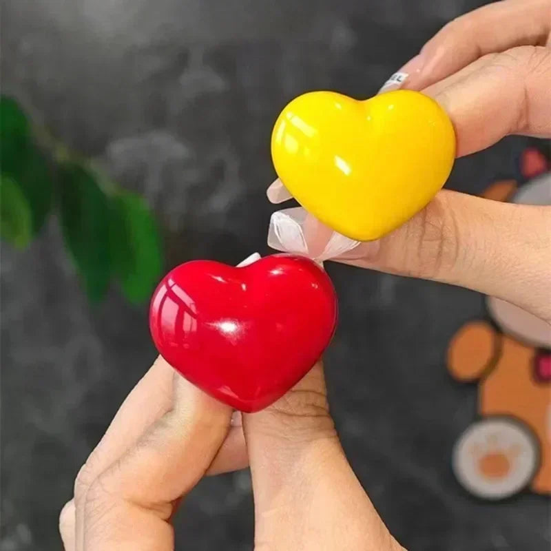 A hand is holding a yellow heart-shaped toilet presser button and a red heart-shaped toilet presser button.