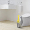 A yellow natural pumice toilet cleaning brush with a handle is shown next to a white toilet bowl and sink area.