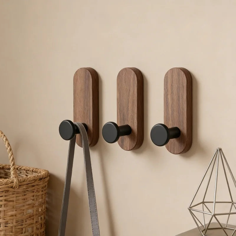 Three dark brown walnut wood wall hooks with a metal hanger are mounted on a beige wall.