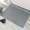 Una estera de ducha de PVC gris antideslizante con numerosos orificios de drenaje sobre una superficie de azulejos.