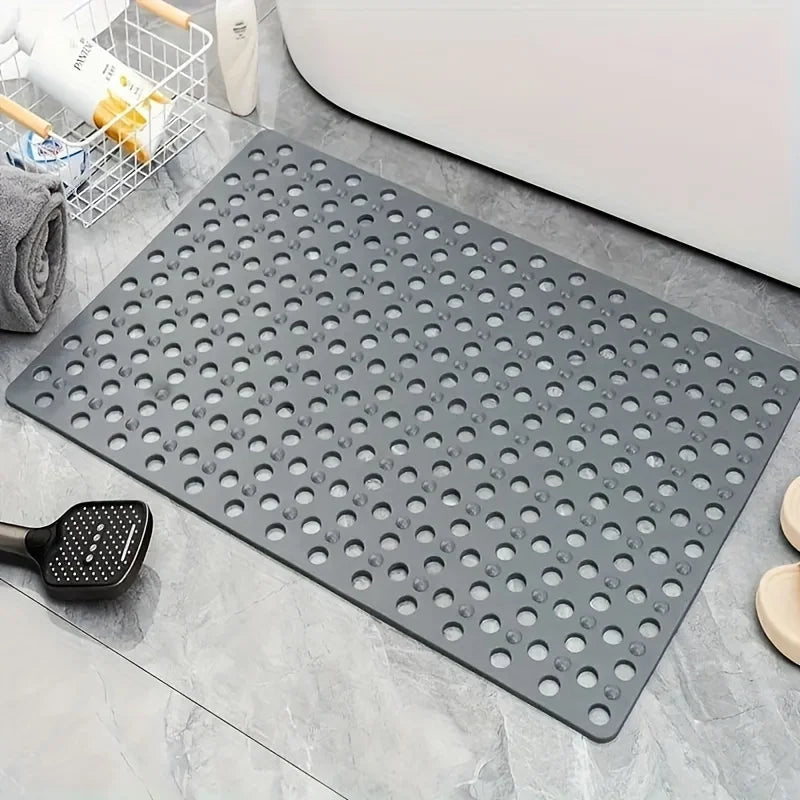 Una estera de ducha de PVC gris antideslizante con numerosos orificios de drenaje sobre una superficie de azulejos.