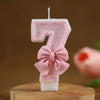 A pink glitter number seven candle tied with a pink bow on a wooden surface.