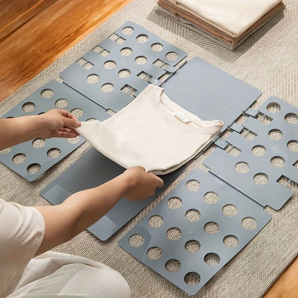 Hands are folding a white garment onto a plastic clothes folding board for laundry organization.