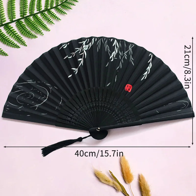 Black folding hand fan with white leaf design shown against a pink background.