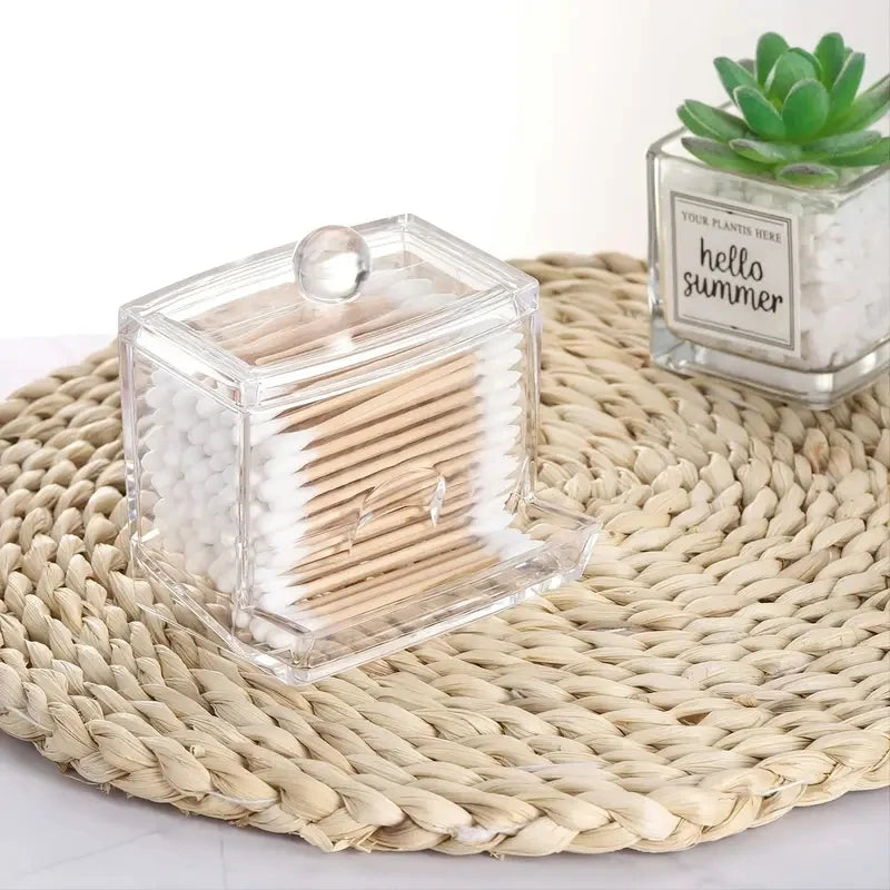 Clear storage box for cotton swabs and pads with a lid resting on a woven mat.