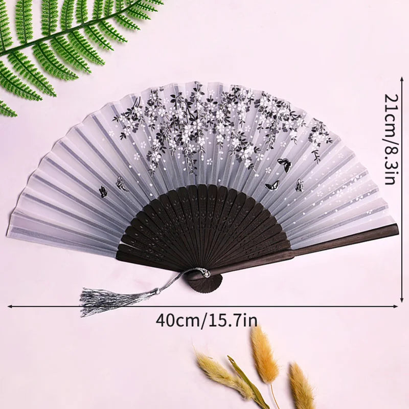 A gray and black lace fabric folding hand fan displayed against a white background with green foliage.