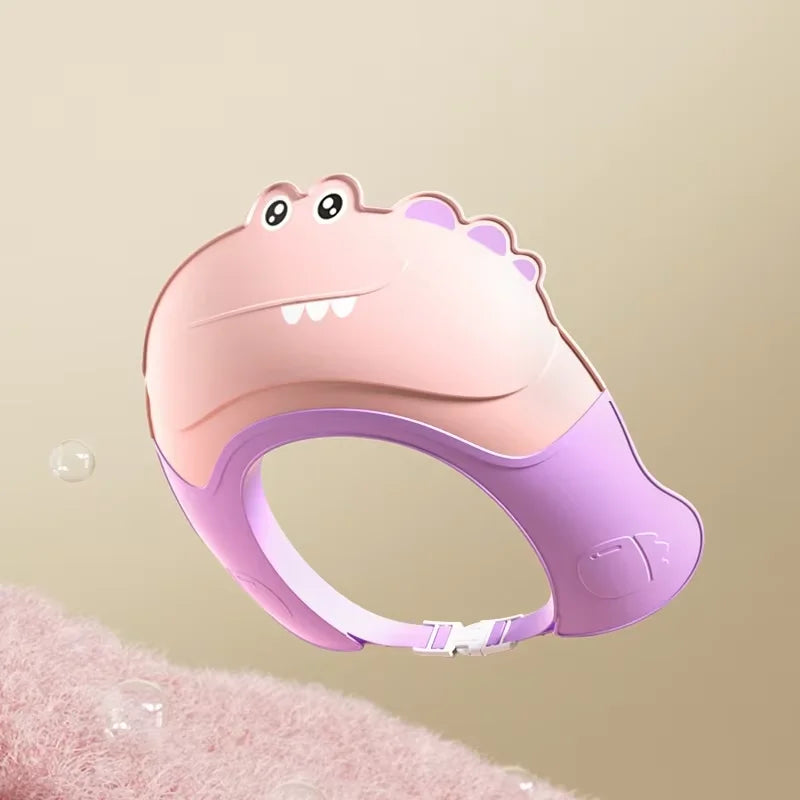 A pink and purple adjustable baby bath shampoo shield cap is shown against a soft pink background.