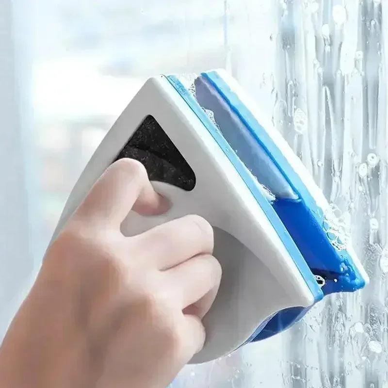A hand is using a white and blue dual-sided magnetic window cleaner to wipe condensation off a glass window.