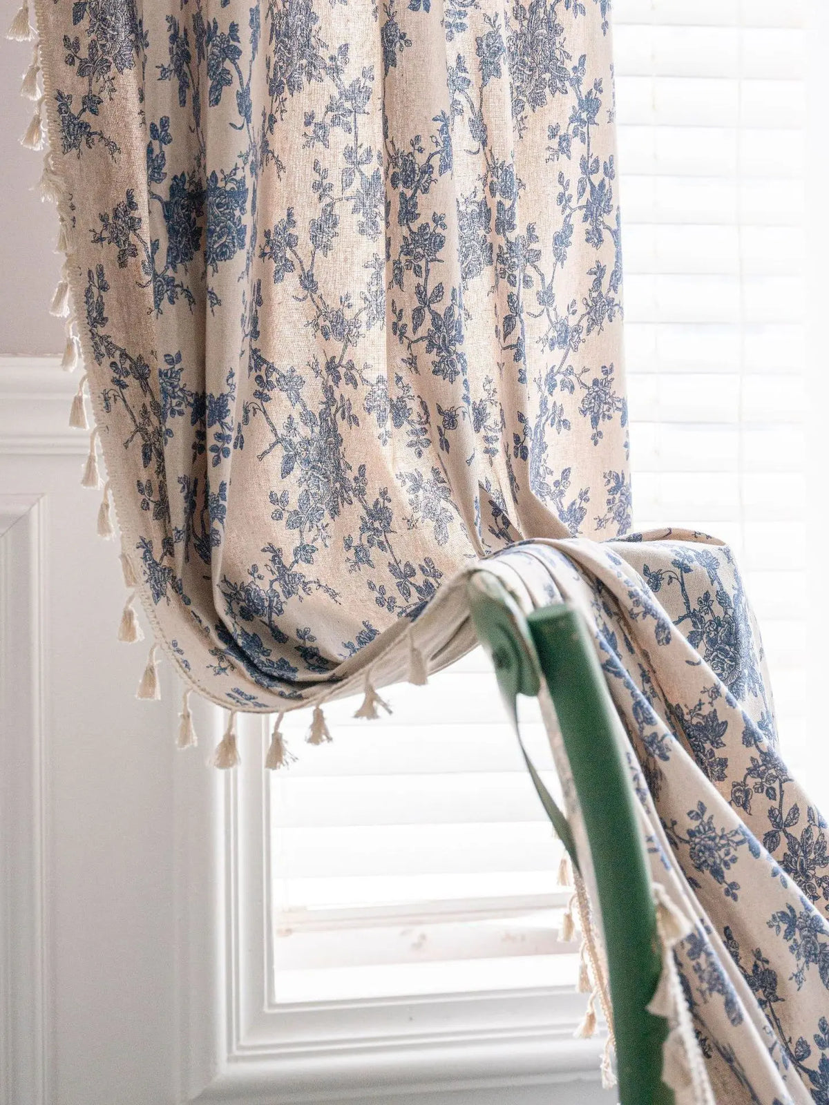Nahaufnahme von Leinen-Blumenvorhängen mit blau-beige Muster und dekorativen Fransen am Fenster.