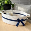 A white woven cotton rope storage basket with navy blue stripes holds a glass candle and is placed on a light wooden surface.