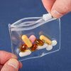 A hand holds a clear plastic organizer bag containing several yellow and pink pills.