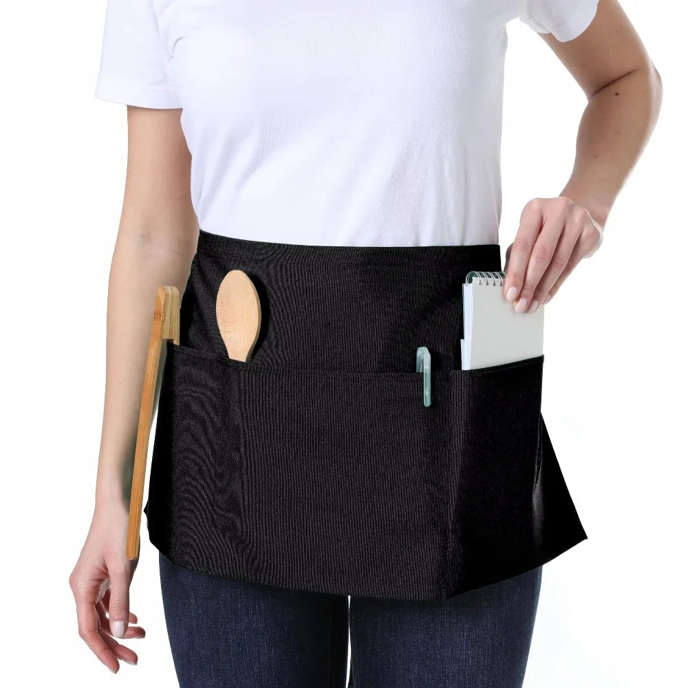 A black fashion chef short apron with pockets is worn by a person.