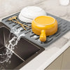 A silicone dish drying mat is shown with a yellow bowl and utensils on it, draining water into a tray below.