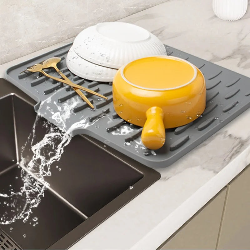 A silicone dish drying mat is shown with a yellow bowl and utensils on it, draining water into a tray below.