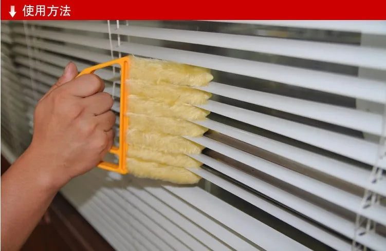 A hand is using an orange tool to clean blinds with a yellow multi-functional brush.