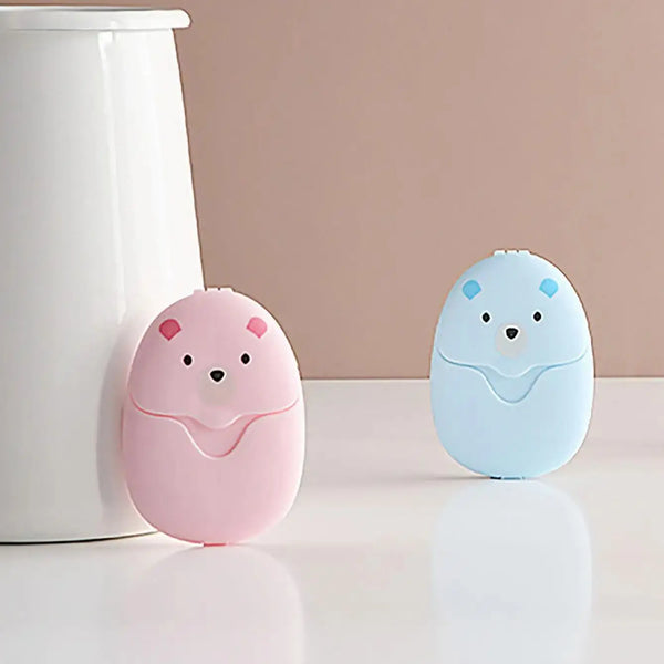Two round, light-colored electronic devices shaped like bears, one pink and one blue, resting on a white surface.