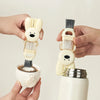 A hand holds a white portable cup and bottle cleaning brush set with a brush and a bunny-shaped grip.