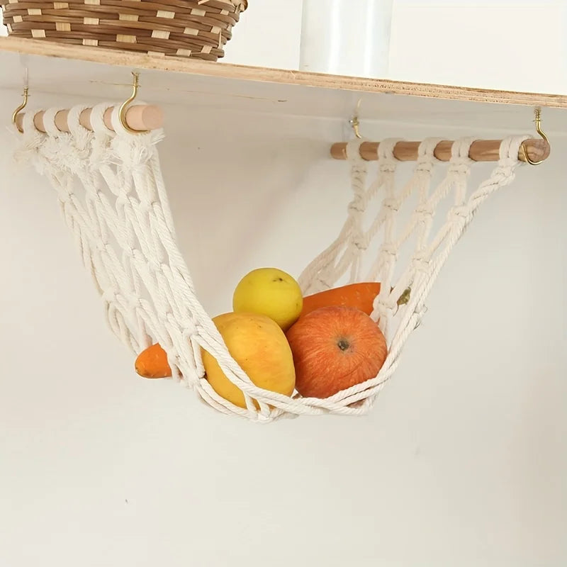 A white macrame fruit hammock made of natural fiber hanging on a wooden shelf.