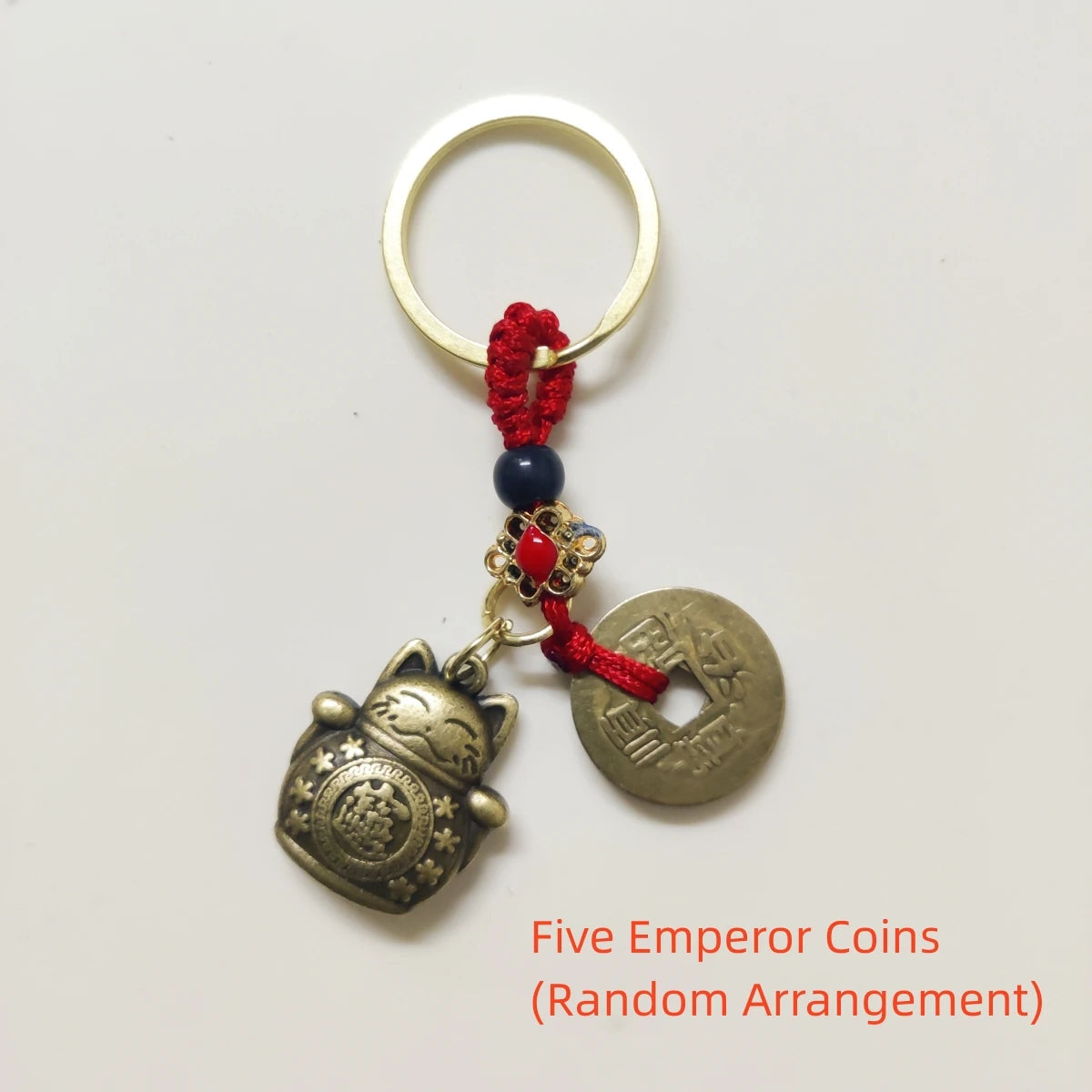 Five emperor coins arranged randomly on a gold-tone keychain with a red tassel.