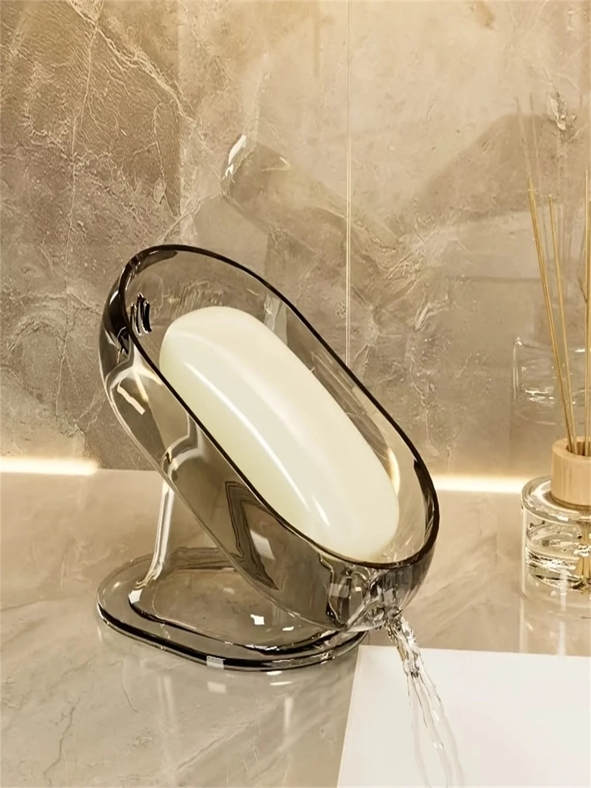 An elegant glass soap dish with a white bar of soap is dripping water onto a marble surface.