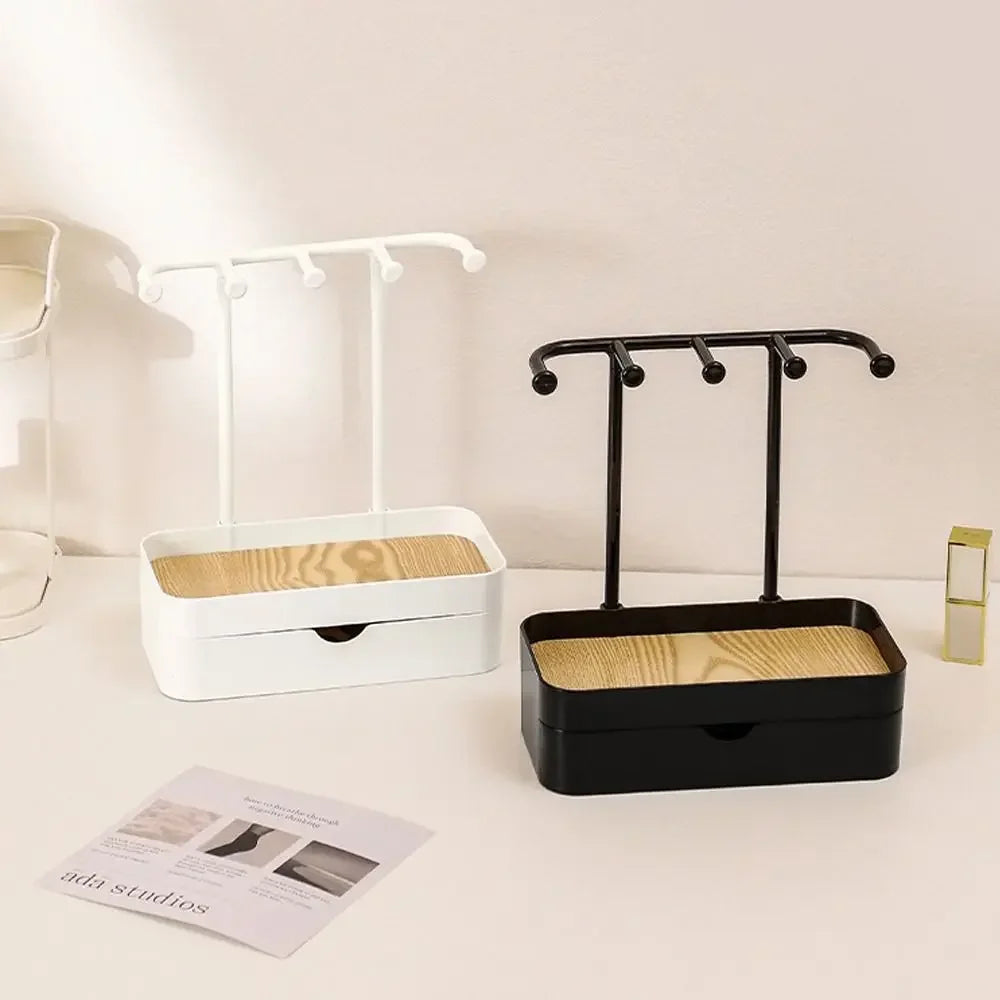 Estante portátil de joyería negro con caja de cajón y estante colgante blanco sobre una superficie clara.