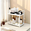 A white two-tier desktop storage rack holding various skincare and cosmetic bottles.